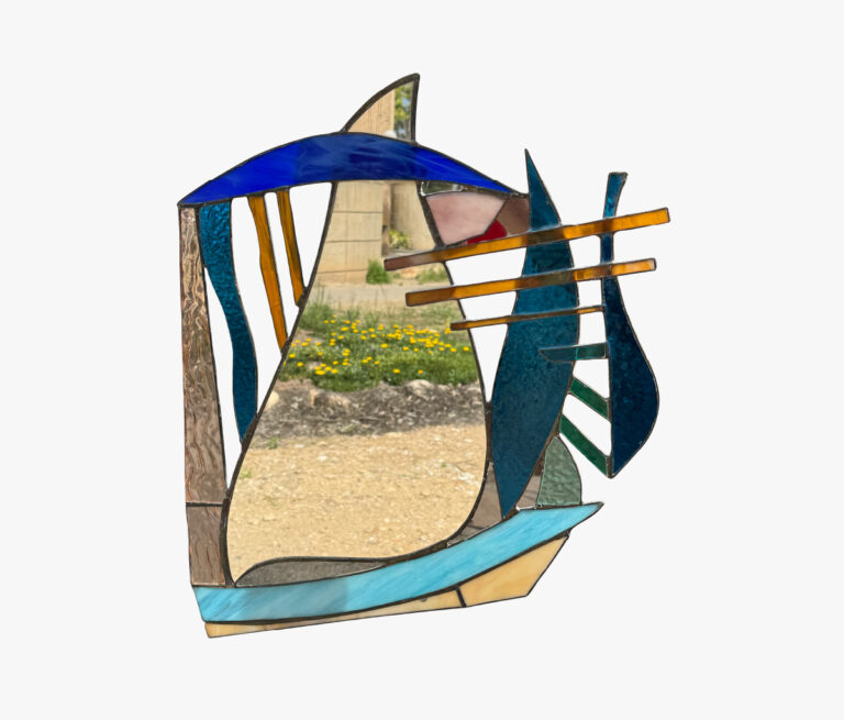 יצירת אמנות מופשטת מזכוכית צבעונית עם צורות מעוגלות וזוויתיות בגווני כחול, צהוב, טורקיז וחום. הזכוכית חצי שקופה, וחושפת שביל, קיר אבן ופרחים צהובים ברקע.