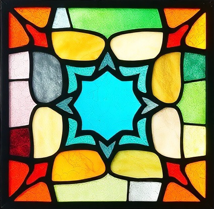 חלון ויטראז' צבעוני עם מרכז בצורת כוכב כחול בוהק, מוקף בחתיכות זכוכית אדומות, צהובות, כתומות, ירוקות, אפורות וקרמיות, היוצרות דפוס גיאומטרי סימטרי.