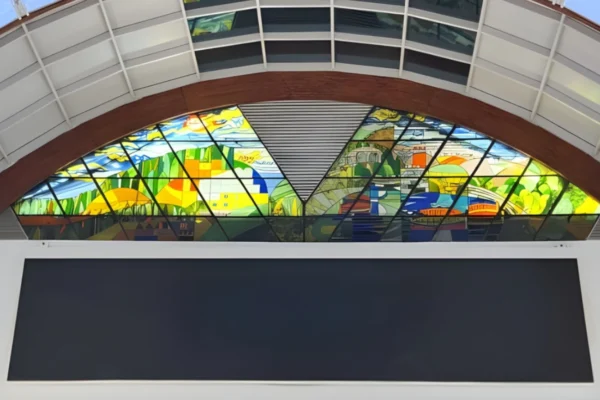 ויטראז' קשתי צבעים בהירים ירוקים ,שמיים עם צבעים צהובים עצים וצמחייה ונהר וכל זה ביצירת ויטראז'.