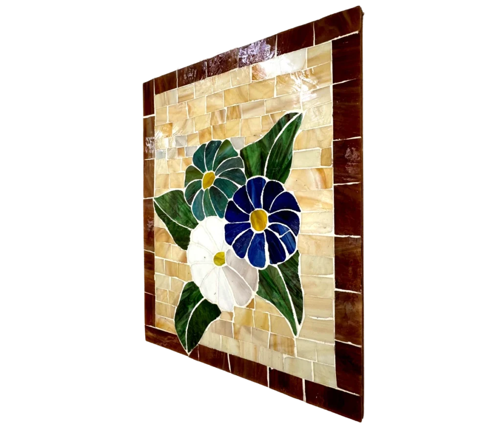 לוח האריחים הקרמי "מבנה של פריחה" מציג שלושה פרחים – שניים כחולים ואחד לבן – עם עלים ירוקים על רקע בז', המוקפים באריחים חומים.