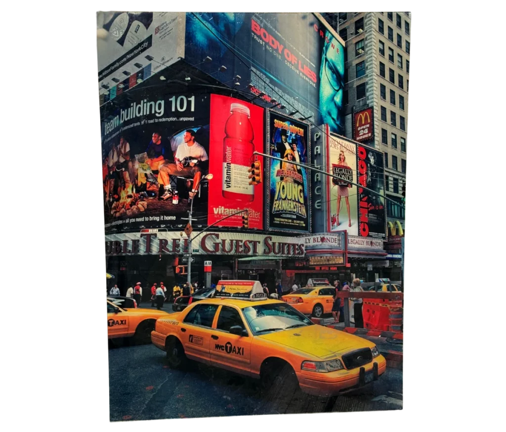 ניו יורק לא עוצרת – מוניות צהובות חוצות את טיימס סקוור הסואן בין גורדי שחקים, שלטי פרסום צבעוניים וניאונים, בהם מקדונלד'ס ו-vitaminwater. הולכי רגל מהלכים על המדרכות.