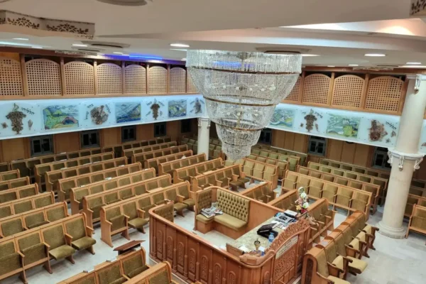 פנים בית הכנסת המרווח, עם שורות של ספסלי עץ ריקים, בימה מרכזית גדולה ועליה ספרים וחפצי פולחן, קישוטים דקורטיביים על הקירות, ונברשת קריסטל מפוארת התלויה מהתקרה.